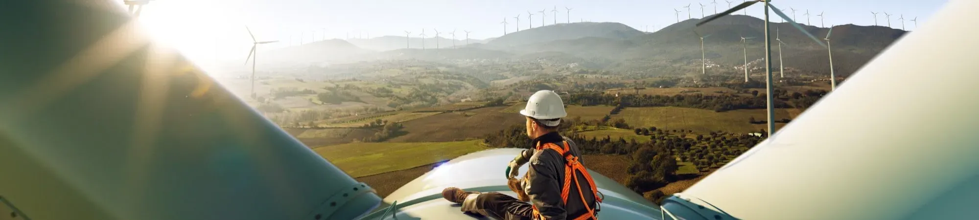 Man sat on wind turbine looking out at fields 